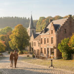 Couple se promenant sur une rue pavée dans un village belge pittoresque en automne, avec église et maisons traditionnelles.