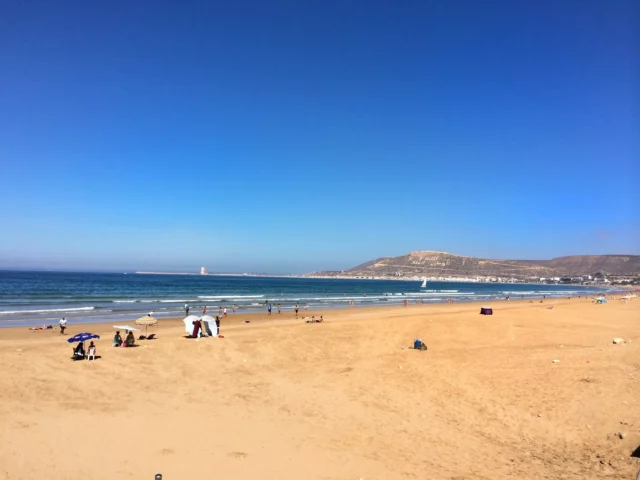 Grande plage ensoleillée d'Agadir sous un ciel bleu, face à la colline d'Oufella, destination soleil proche de la Belgique