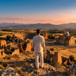 Un homme de dos observe un paysage italien vallonné avec ruines antiques, un amphithéâtre et une église, au coucher du soleil.