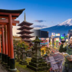 Couple de touristes avec carte et appareil devant des torii, une pagode, une ville moderne et le Mont Fuji.