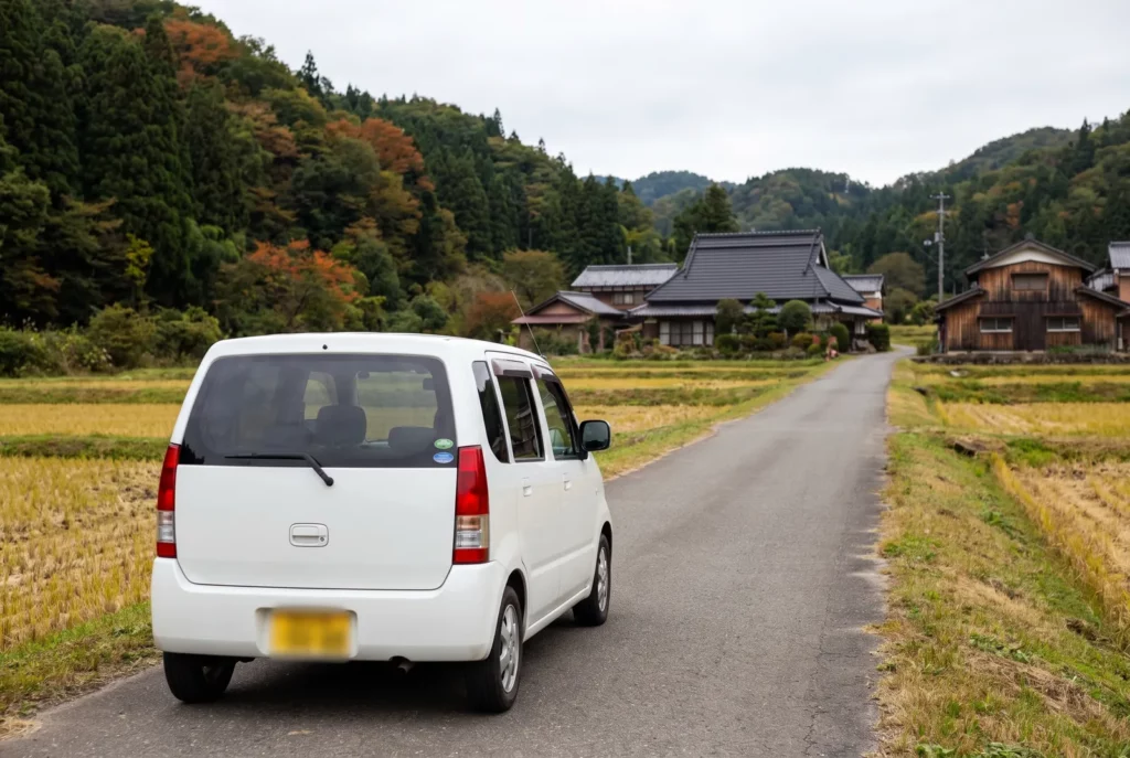 Petite voiture de location roulant à gauche sur une route de campagne japonaise bordée de rizières, au Japon