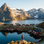 Vue sur le village de Reine aux Lofoten: maisons rouges, fjord calme, montagnes enneigées. Un homme contemple le paysage.