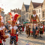 Participants en costume traditionnel de Gilles et géants défilant sur une place pavée lors d'un festival en Belgique.