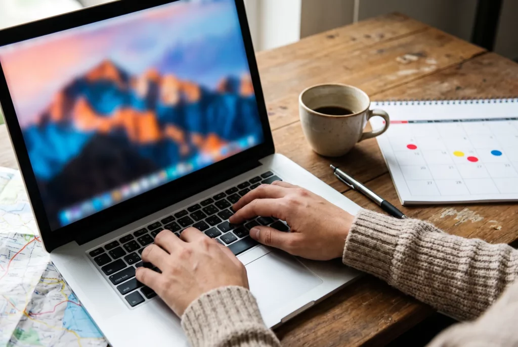 Mains sur un ordinateur portable près d'un café et d'un calendrier, pour comparer les vols directs depuis Bruxelles