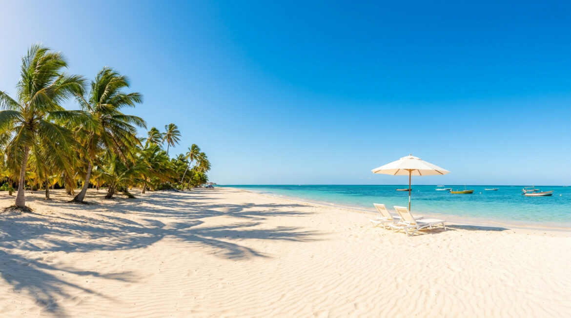 Une plage de sable blanc avec des chaises longues, un parasol et des palmiers au bord d'une mer turquoise.