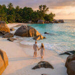 Un couple se tenant la main sur une plage paradisiaque aux Seychelles au coucher du soleil, entouré de rochers granitiques.